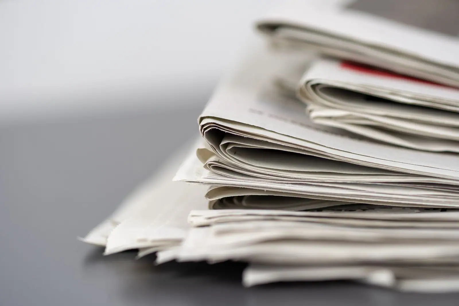 Pile de journaux imprimés pliés posés sur une surface neutre, image illustrant le suivi de l'information