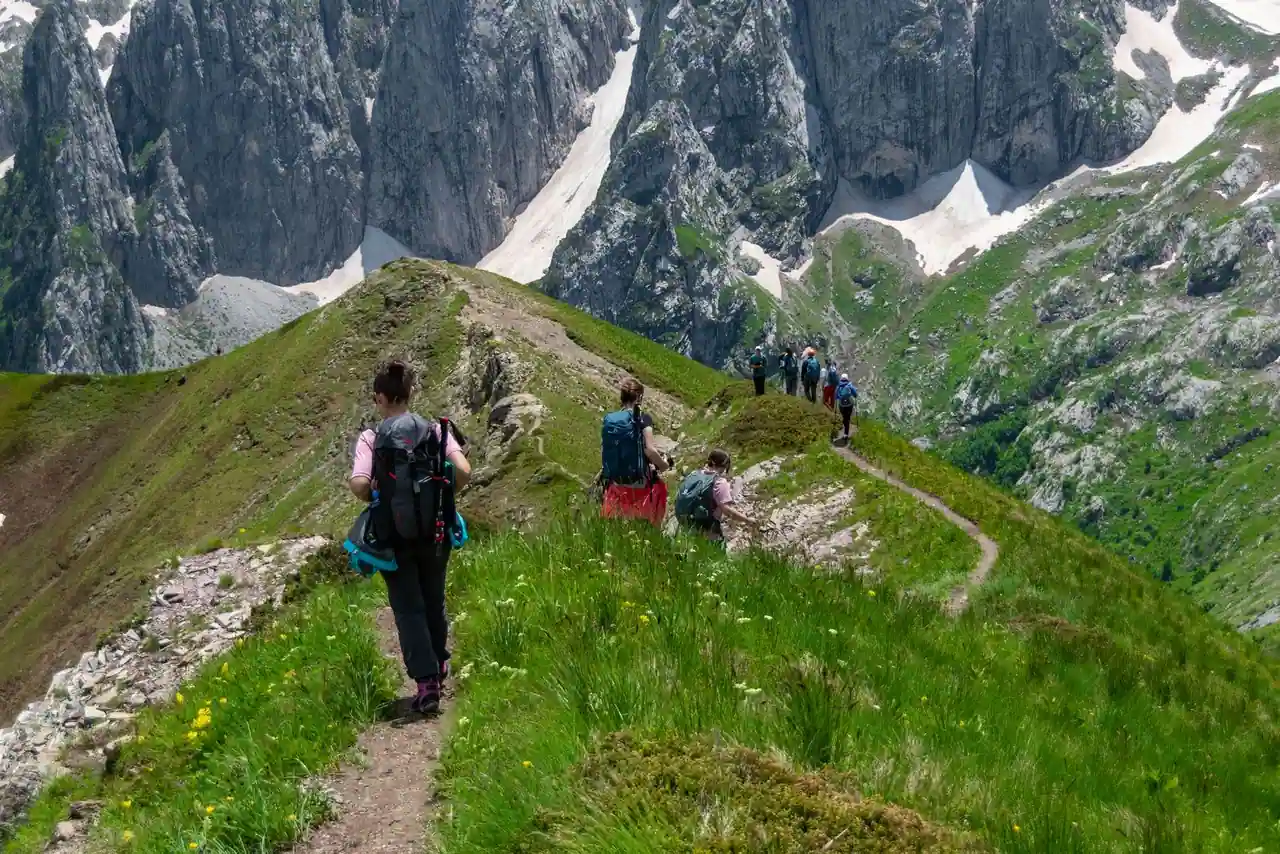 Randonneurs marchant en file sur un sentier de crête entouré de montagnes verdoyantes