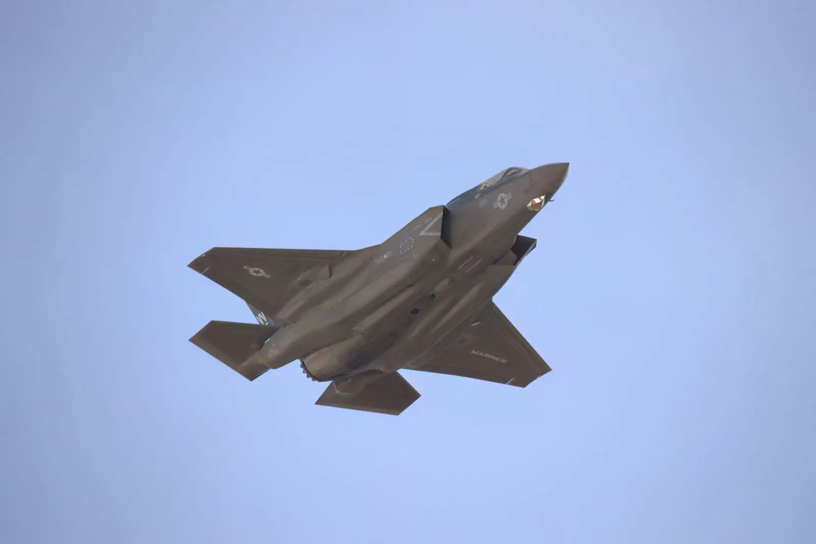 Avion militaire furtif aux lignes anguleuses survolant un ciel dégagé en plein jour