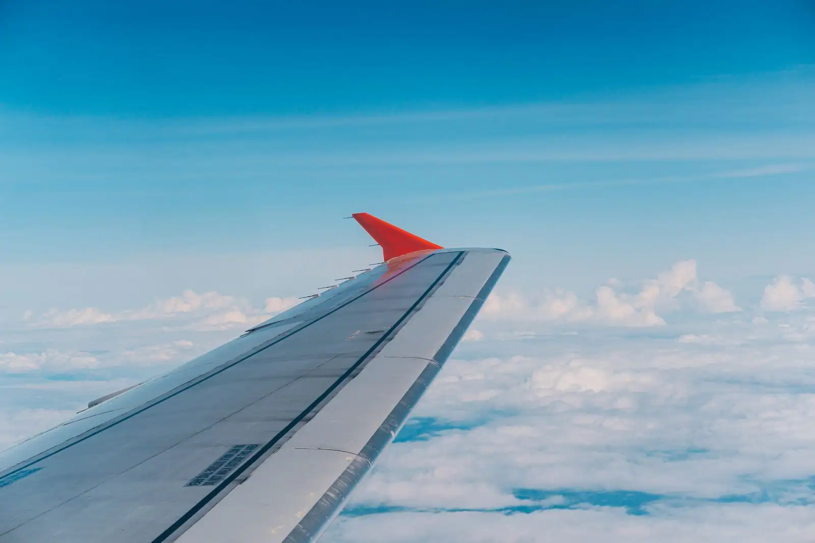 Aile d'un avion de ligne au winglet orange survolant une mer de nuages sous un ciel bleu