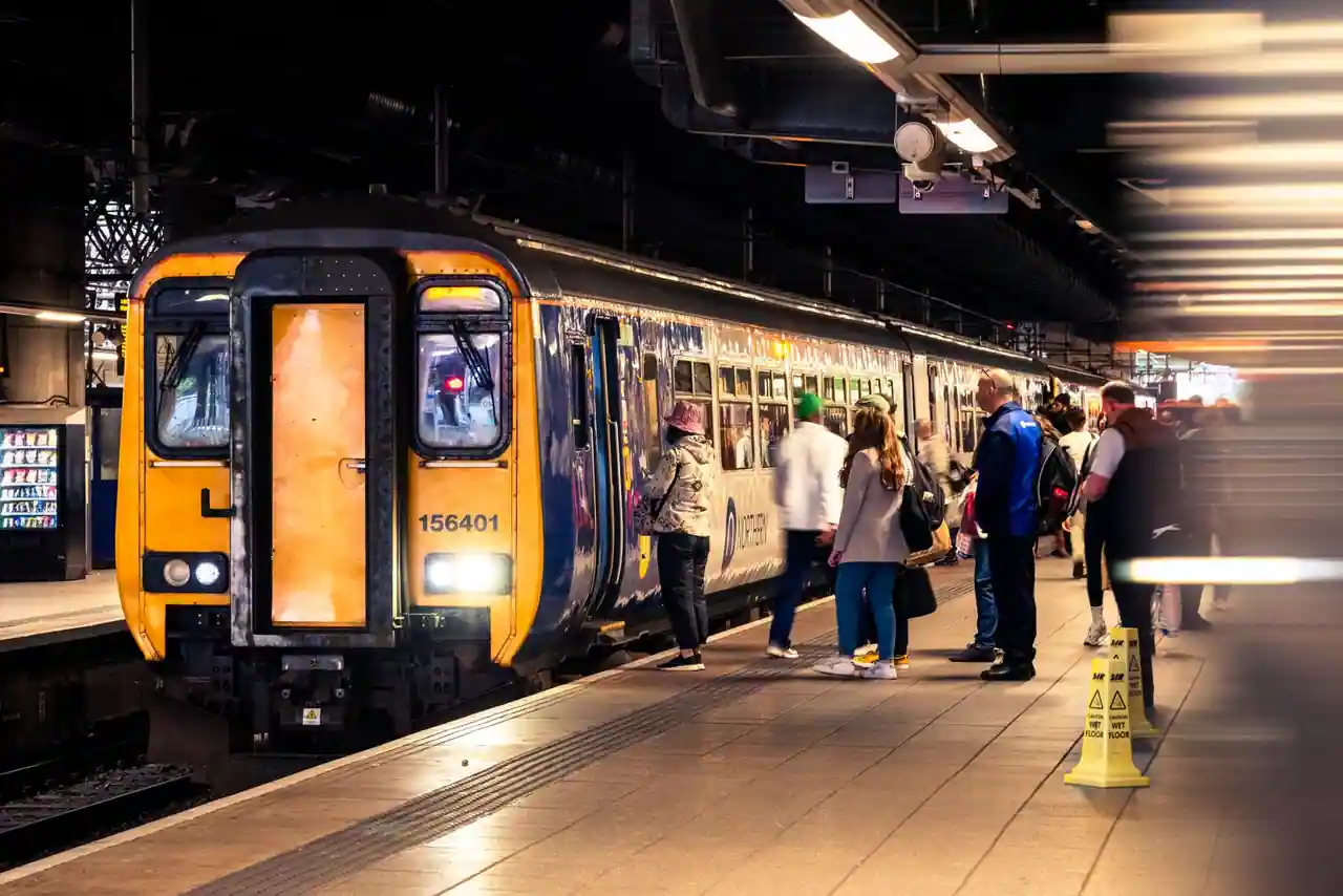Un train à quai dans une gare, des voyageurs attendent sur le quai pour monter à bord.
