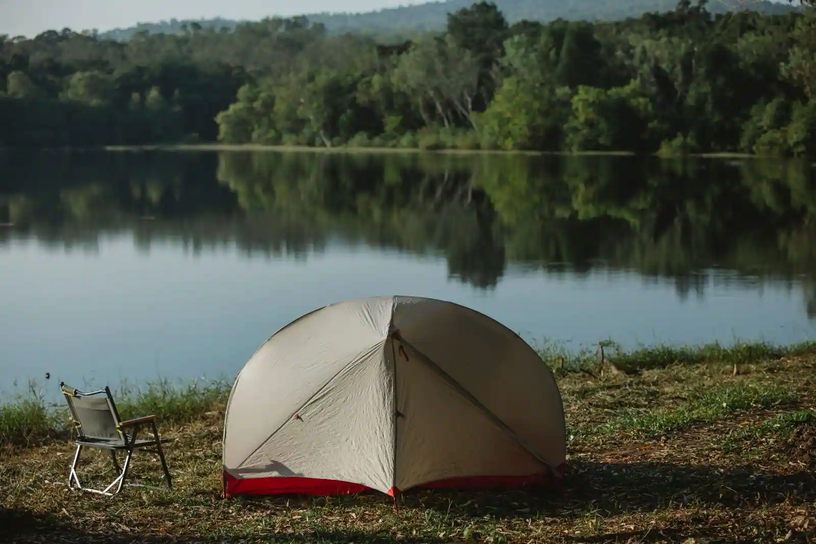 Tente de camping et chaise pliante installées au bord d'une rivière calme
