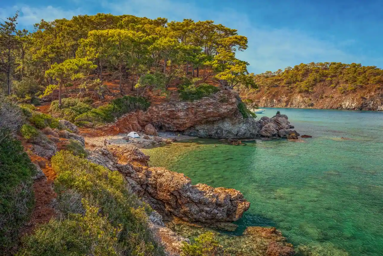 Une tente plantée au bord d'une crique méditerranéenne aux eaux turquoise.