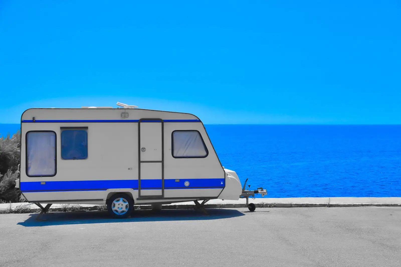 Une caravane de camping stationnée face à la mer Méditerranée, sous un ciel d'été dégagé.
