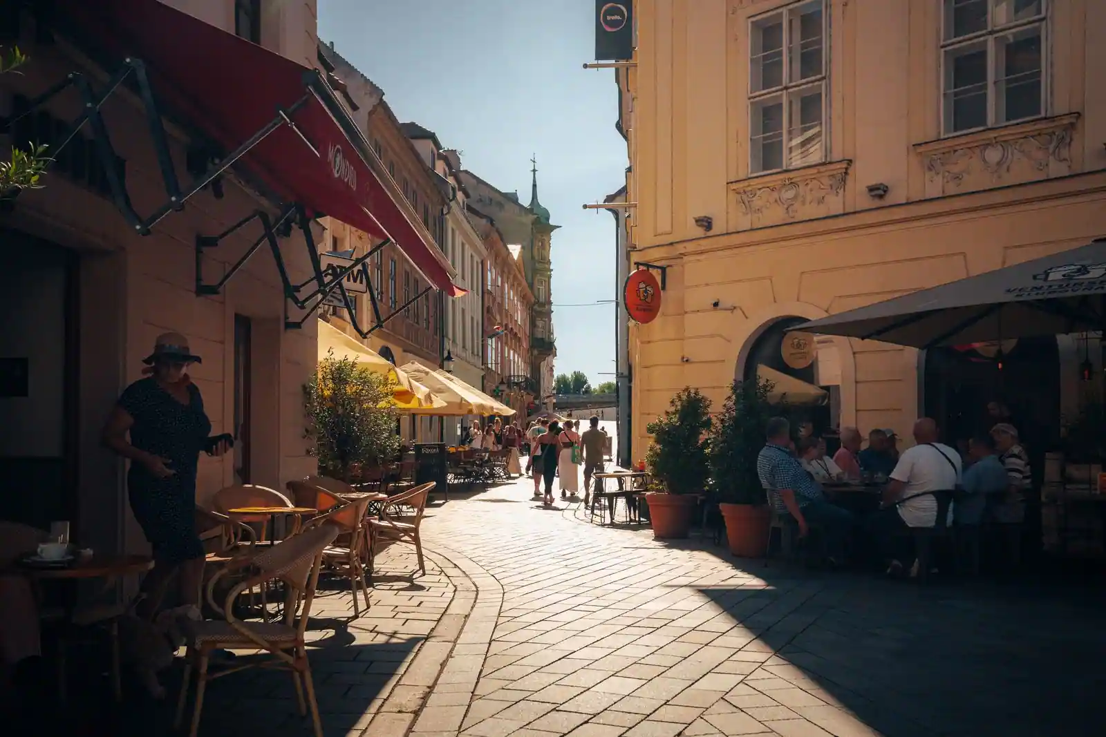 Rue piétonne animée d'une vieille ville européenne avec terrasses de café au soleil