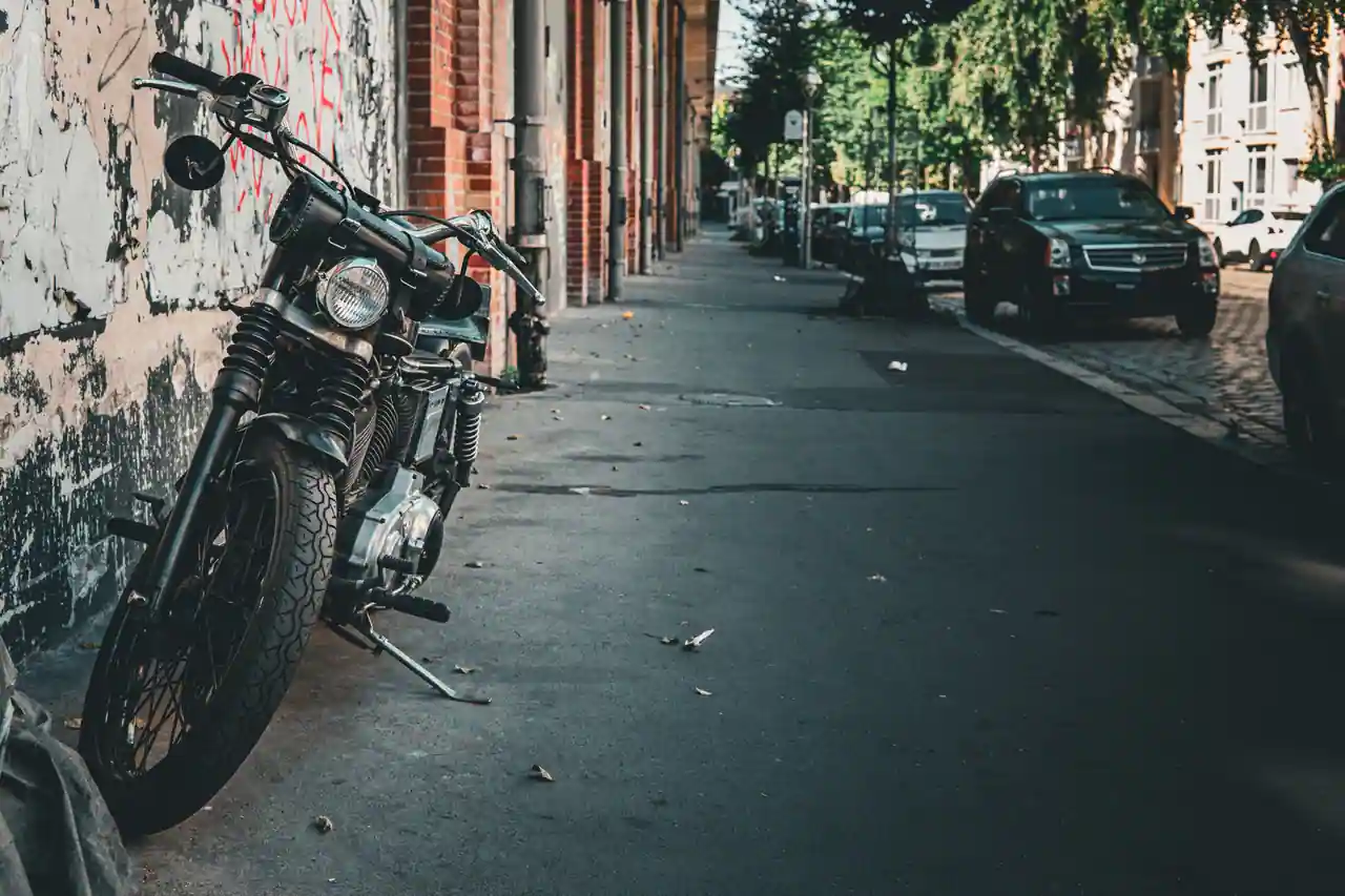 Moto classique stationnée le long d'un trottoir, vue de profil, contre un mur dans une rue urbaine.