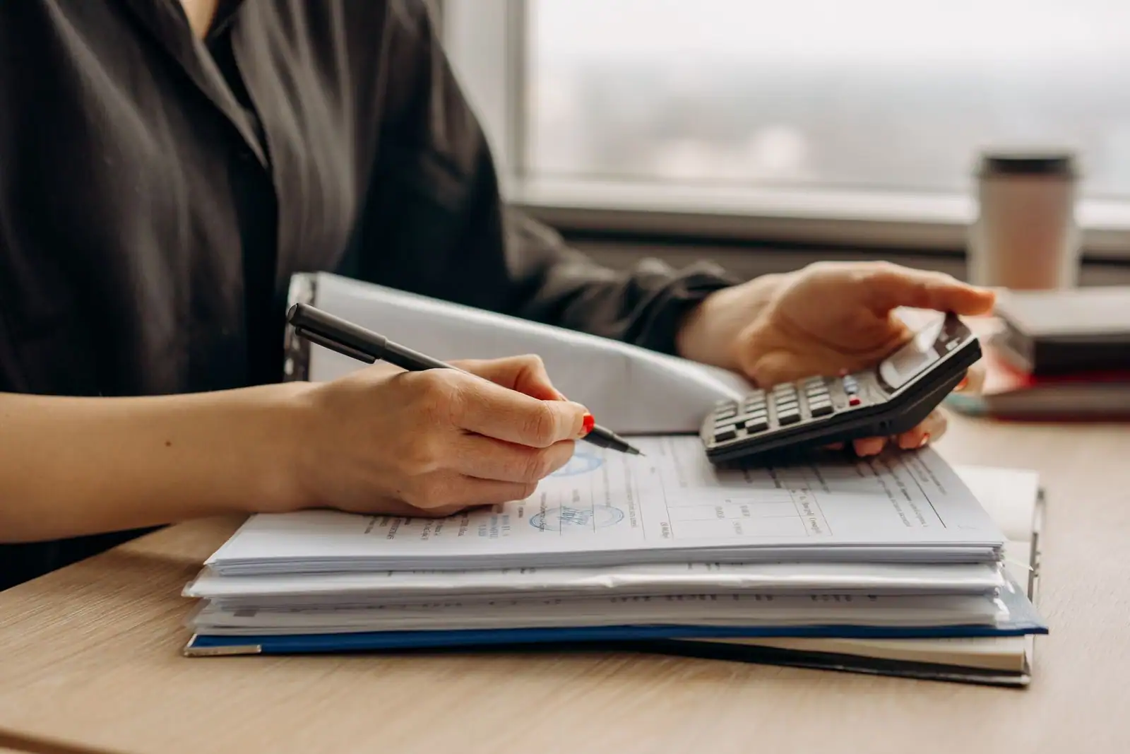 Personne examinant une pile de documents financiers avec un stylo et une calculatrice sur un bureau