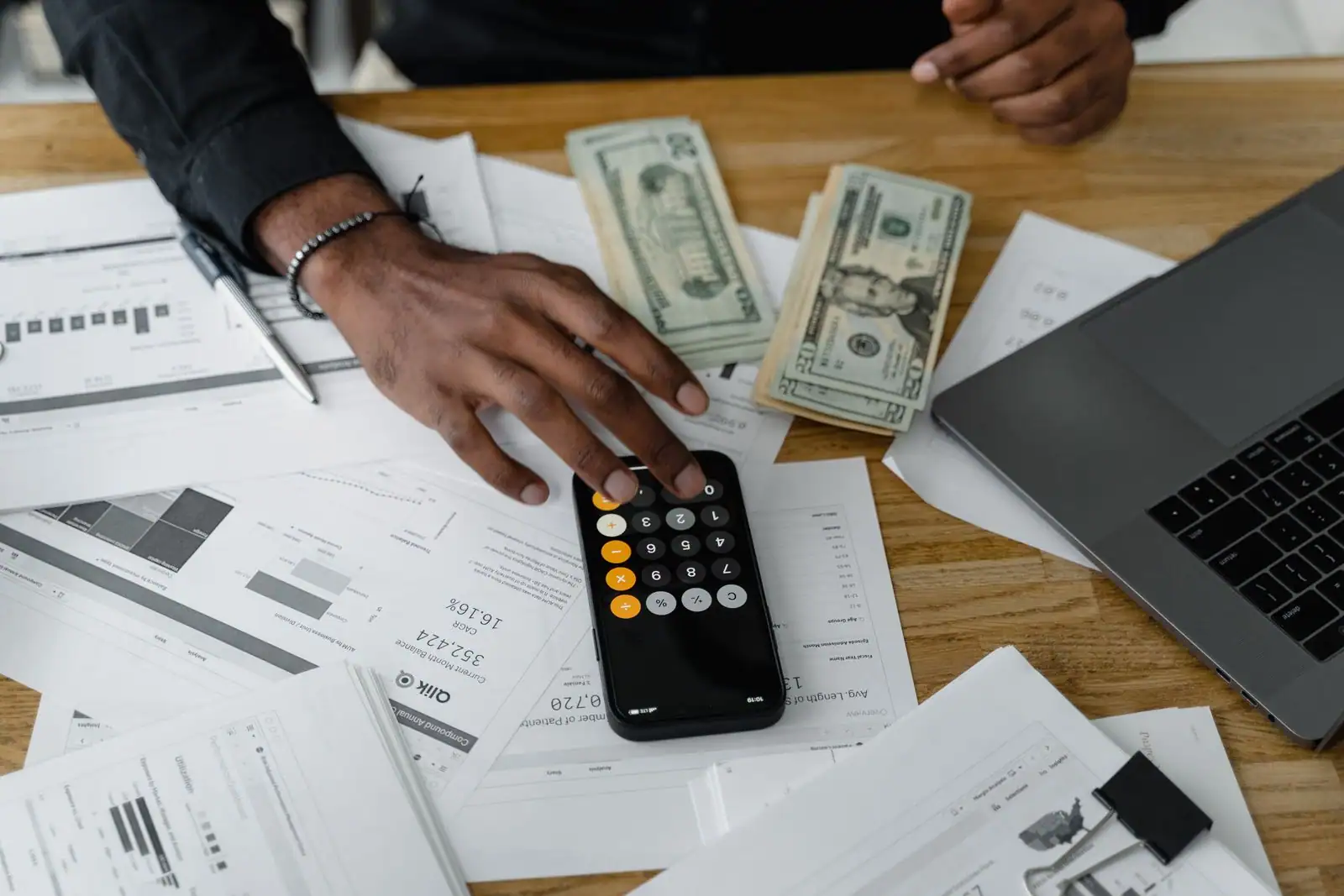 Personne comparant des offres bancaires sur un ordinateur portable avec des documents et une calculatrice