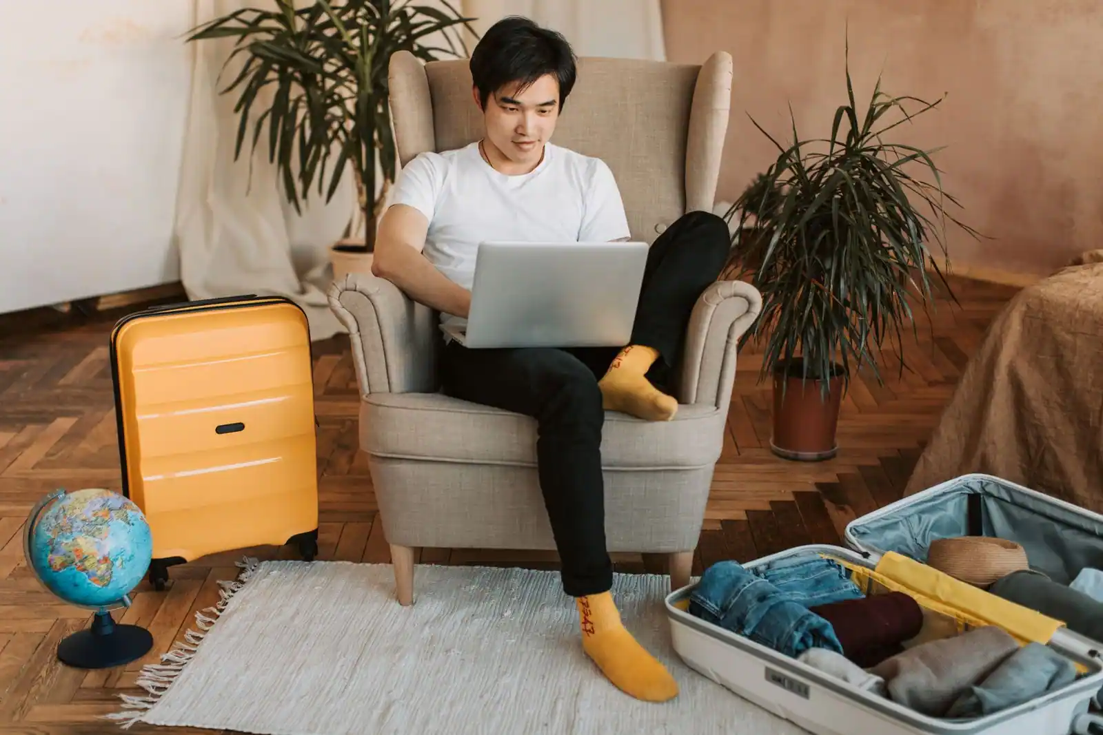 Voyageur comparant des offres sur son ordinateur portable, valise ouverte et globe à proximité