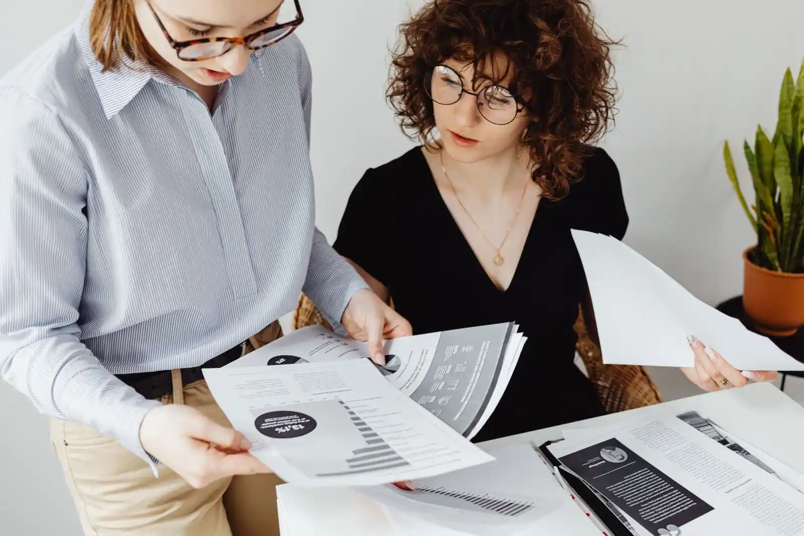 Deux femmes examinent ensemble des documents imprimés et comparent le contenu de plusieurs pages.