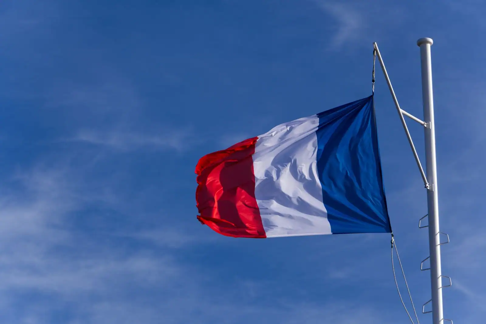 Drapeau français tricolore flottant au sommet d'un mât, sur fond de ciel bleu