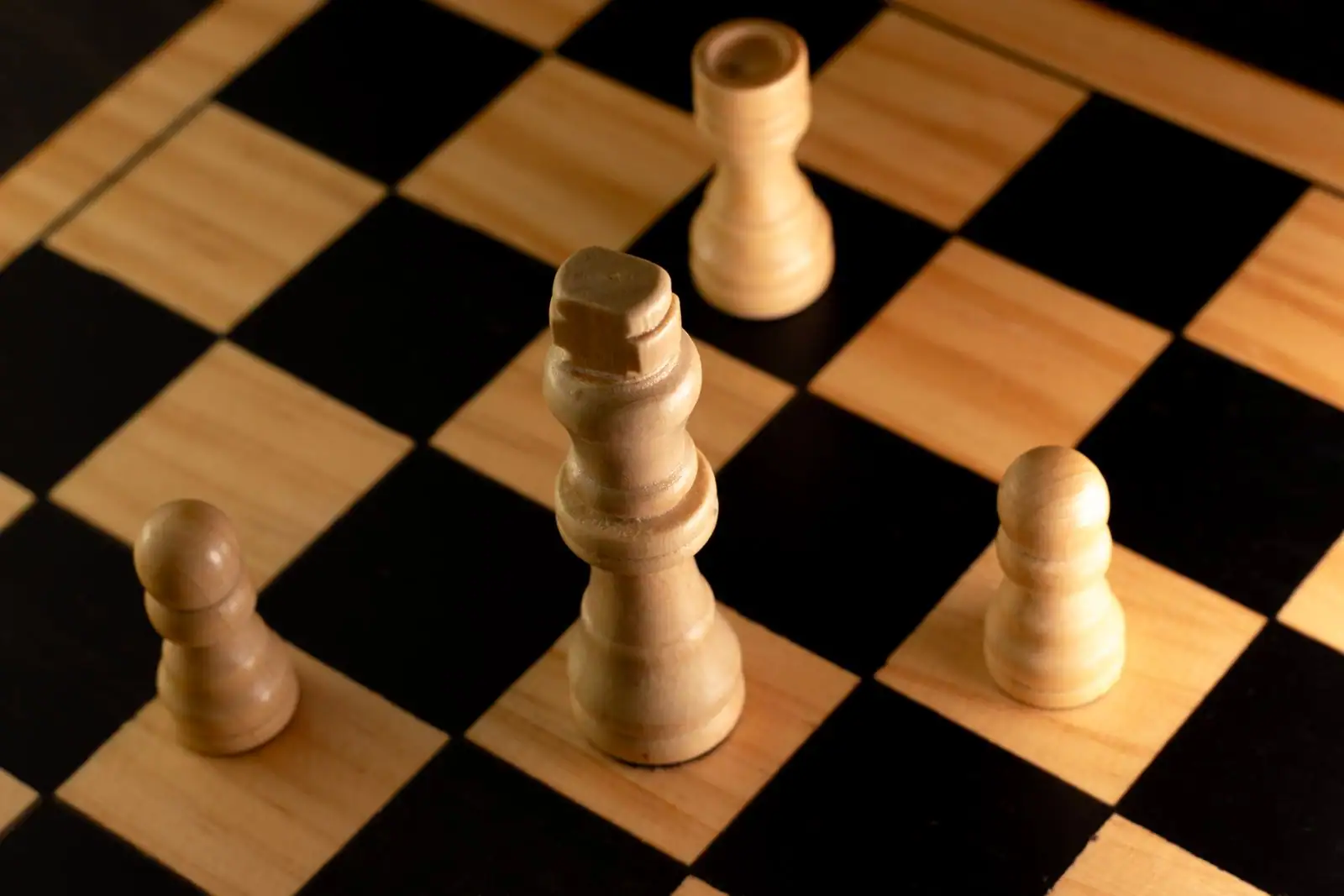 Quelques pièces d'échecs en bois clair posées sur un échiquier en damier, vues en gros plan