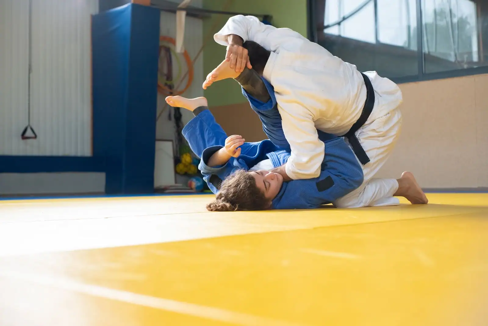 Deux judokas, l'un en kimono blanc l'autre en bleu, lors d'un travail au sol sur un tatami jaune