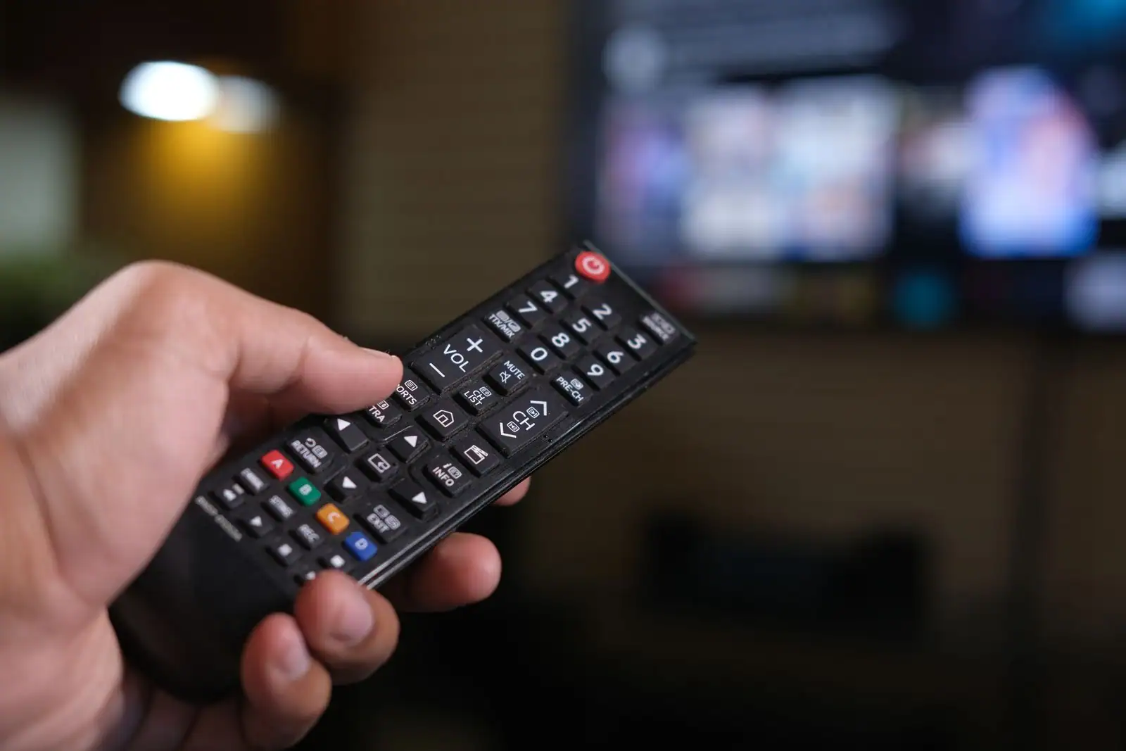 Main tenant une télécommande de télévision face à un écran de téléviseur allumé dans un salon
