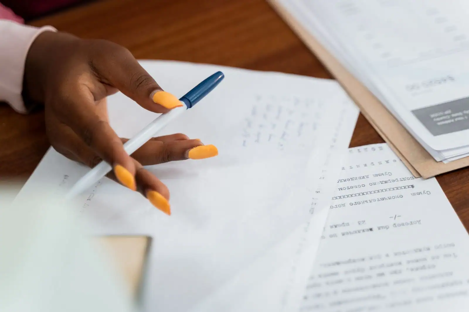 Main tenant un stylo au-dessus de plusieurs documents administratifs posés sur un bureau