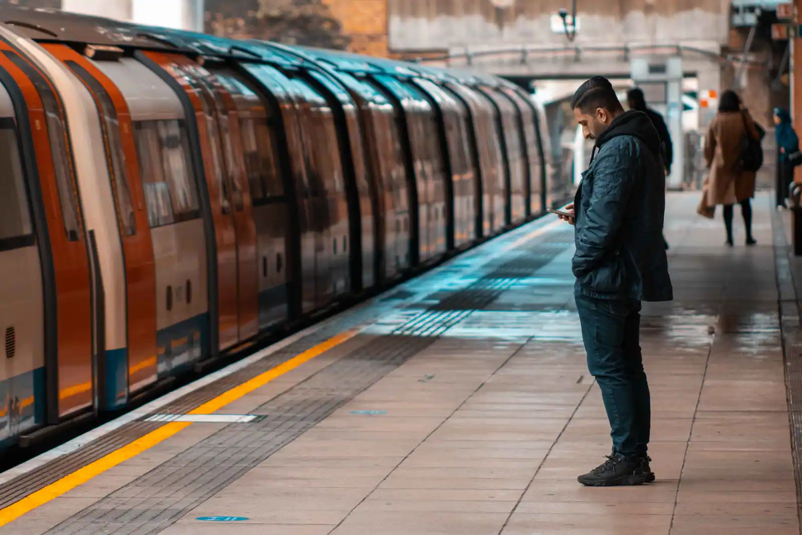 Voyageur consultant son téléphone sur un quai de gare pendant qu'un train arrive le long du quai