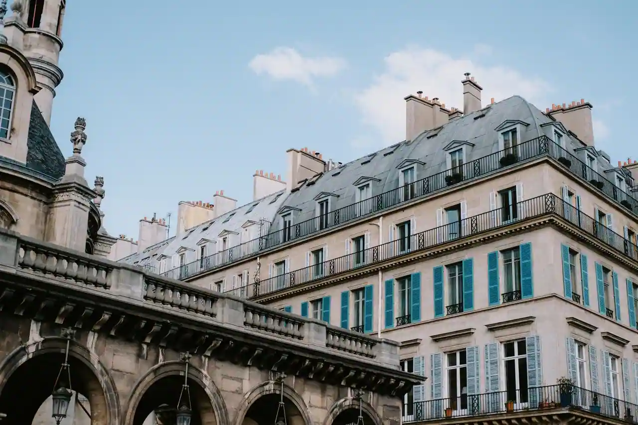 Façade d'immeuble haussmannien parisien en pierre claire, balcons en fer forgé et volets bleus