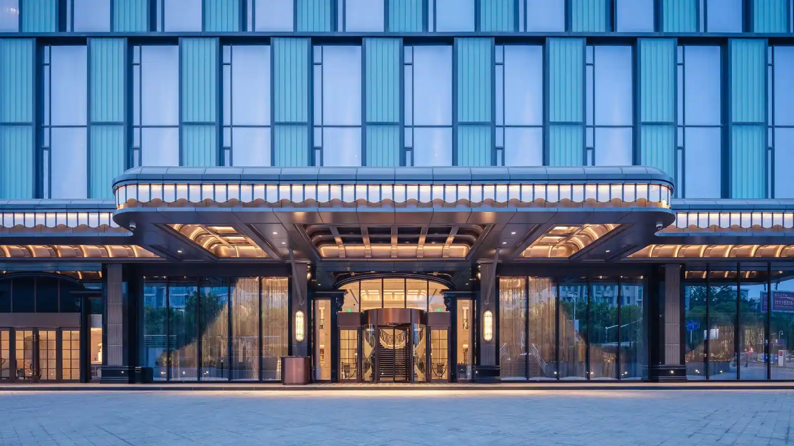 Entrée illuminée d'un hôtel contemporain avec un grand auvent et une façade vitrée en soirée