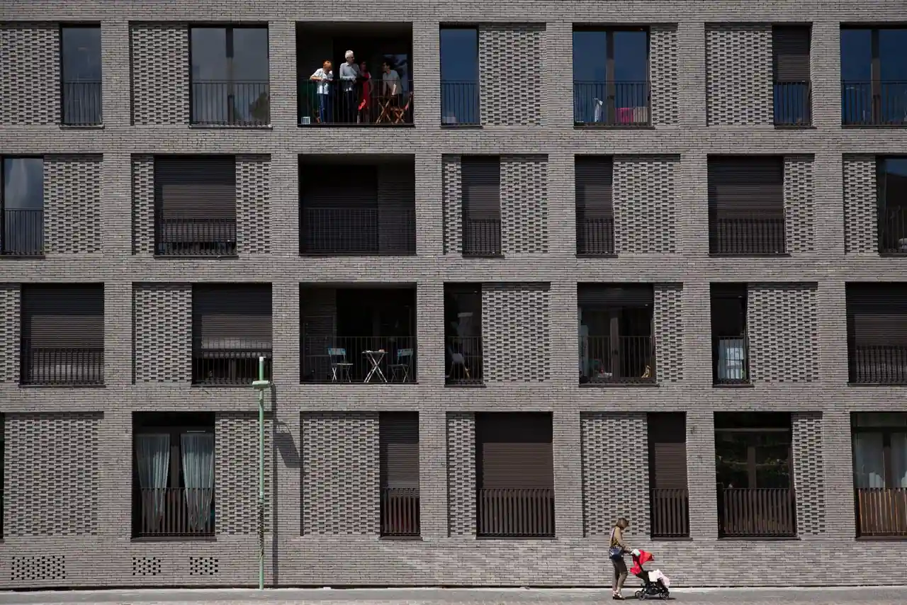Façade d'un immeuble d'habitation moderne, un parent passe avec une poussette sur le trottoir.
