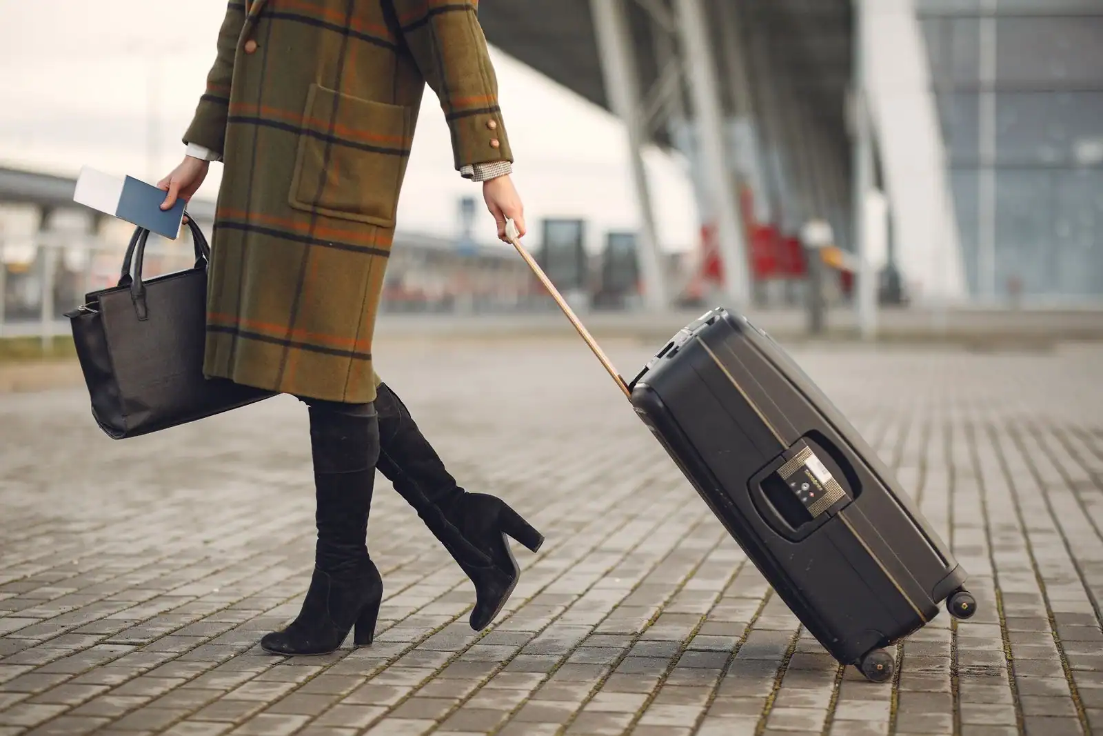 Voyageuse tirant une valise à roulettes devant un terminal d'aéroport, passeport à la main