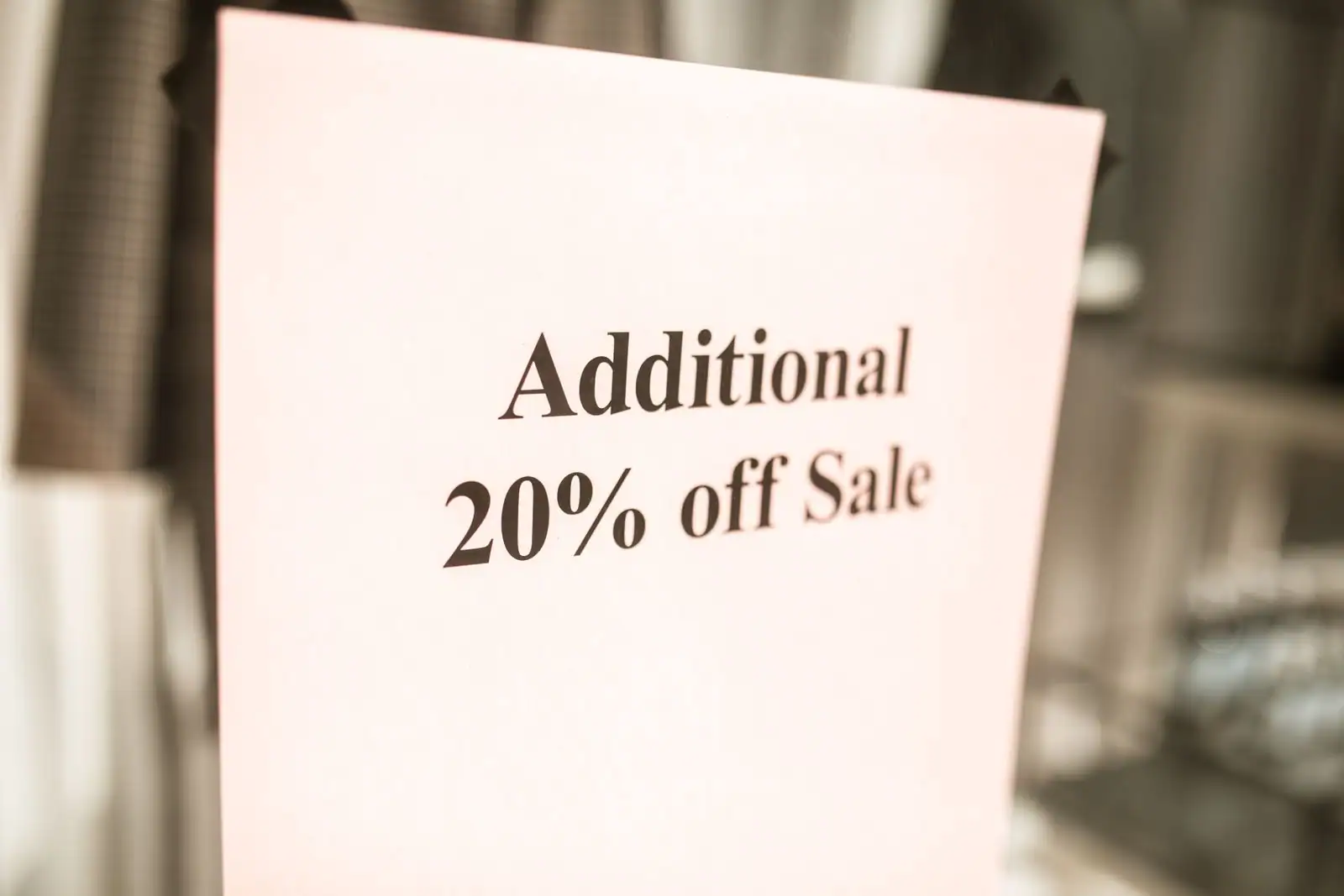 Panneau de réduction en anglais « Additional 20% off Sale » posé devant des vêtements en magasin