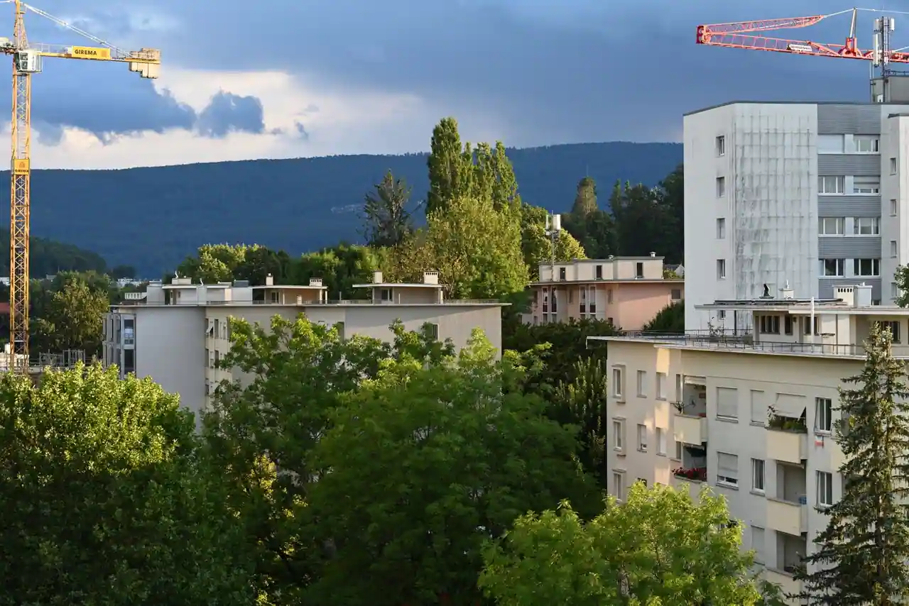 Immeubles d'habitation entourés d'arbres, avec des grues de chantier, dans une ville au pied des collines