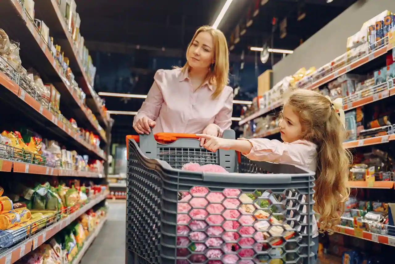 Une femme et une enfant avec un chariot dans l'allée d'un supermarché aux rayons garnis