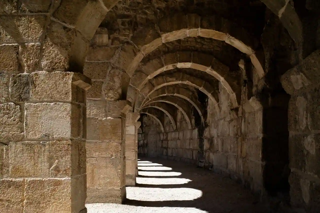 Galerie voûtée d'arches en pierre dans un amphithéâtre romain antique, éclairée par le soleil