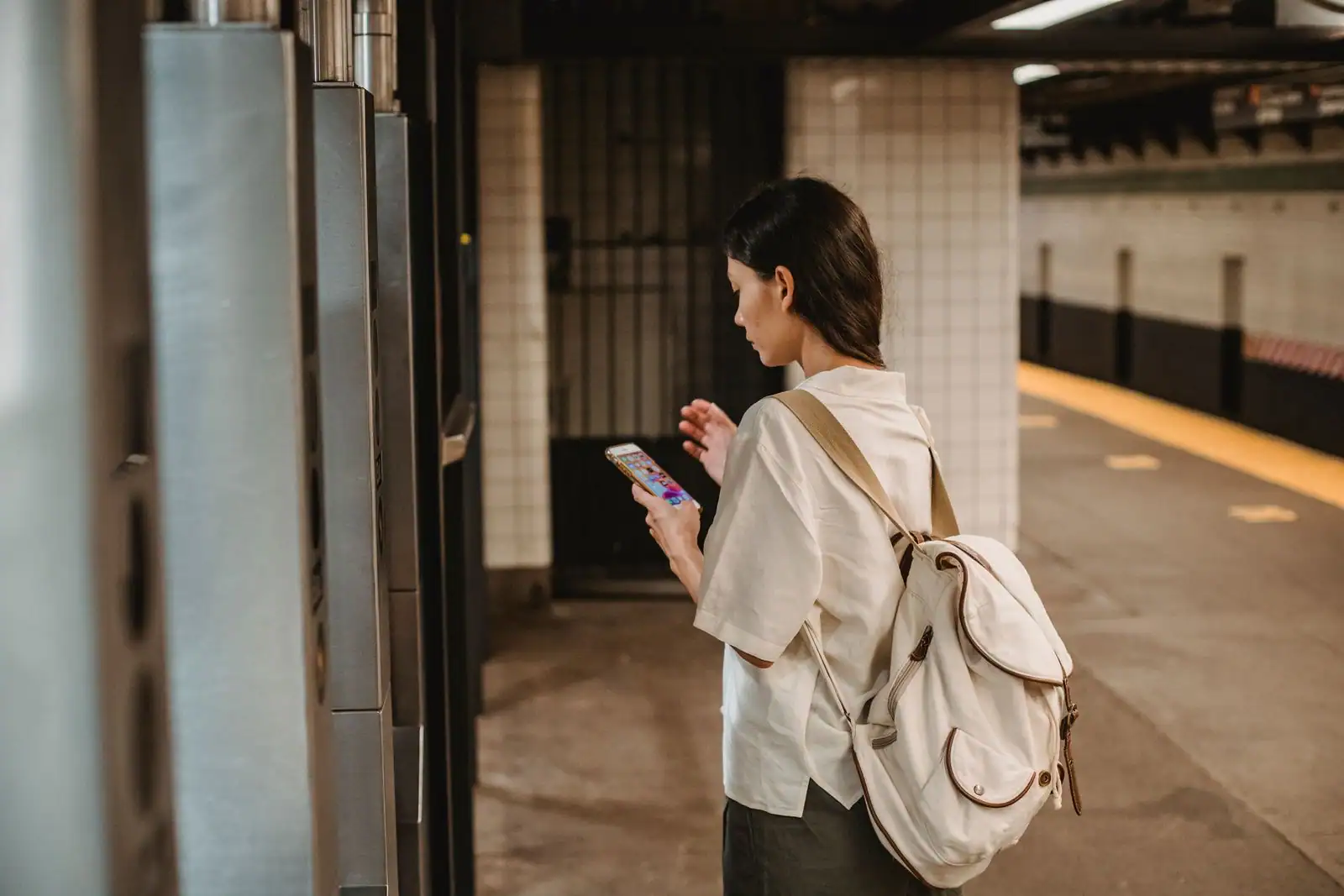 Voyageuse consultant son smartphone sur le quai d'une station, sac au dos.