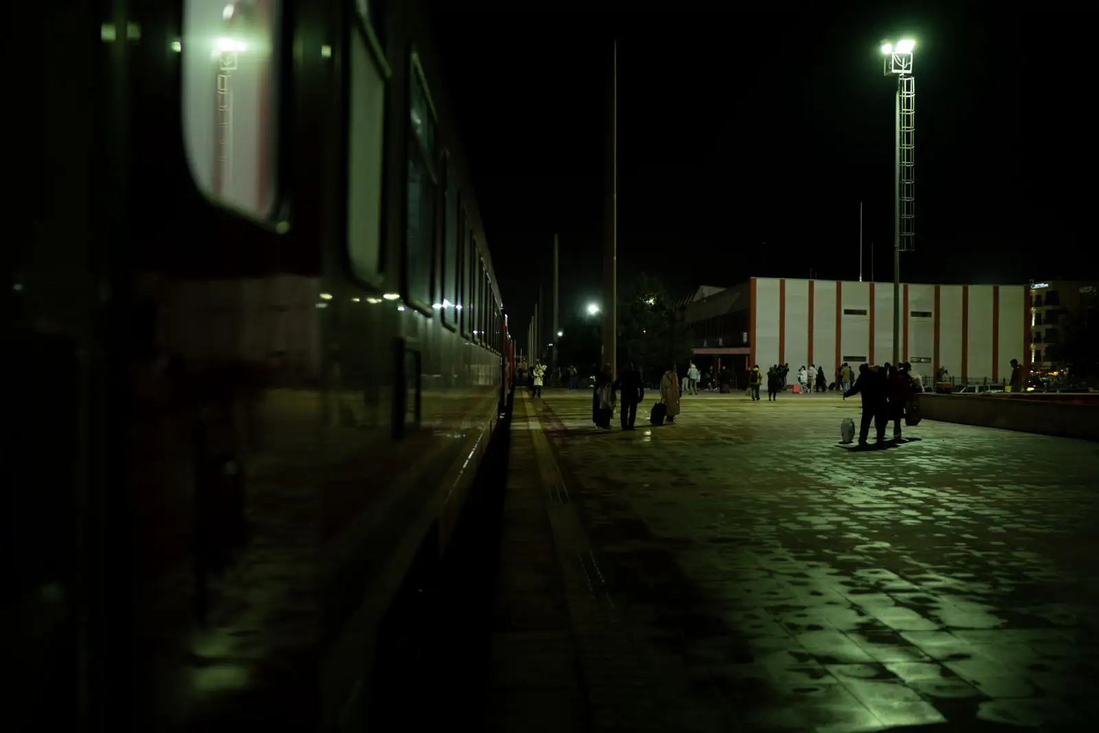 Train de voyageurs le long d'un quai de gare la nuit, avec des voyageurs et leurs bagages.