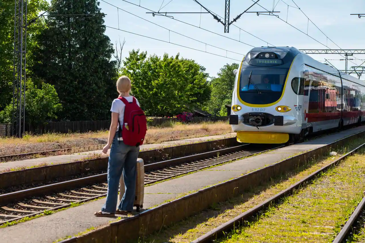 Voyageur avec un sac à dos sur un quai de gare, attendant l'arrivée d'un train régional le long des voies
