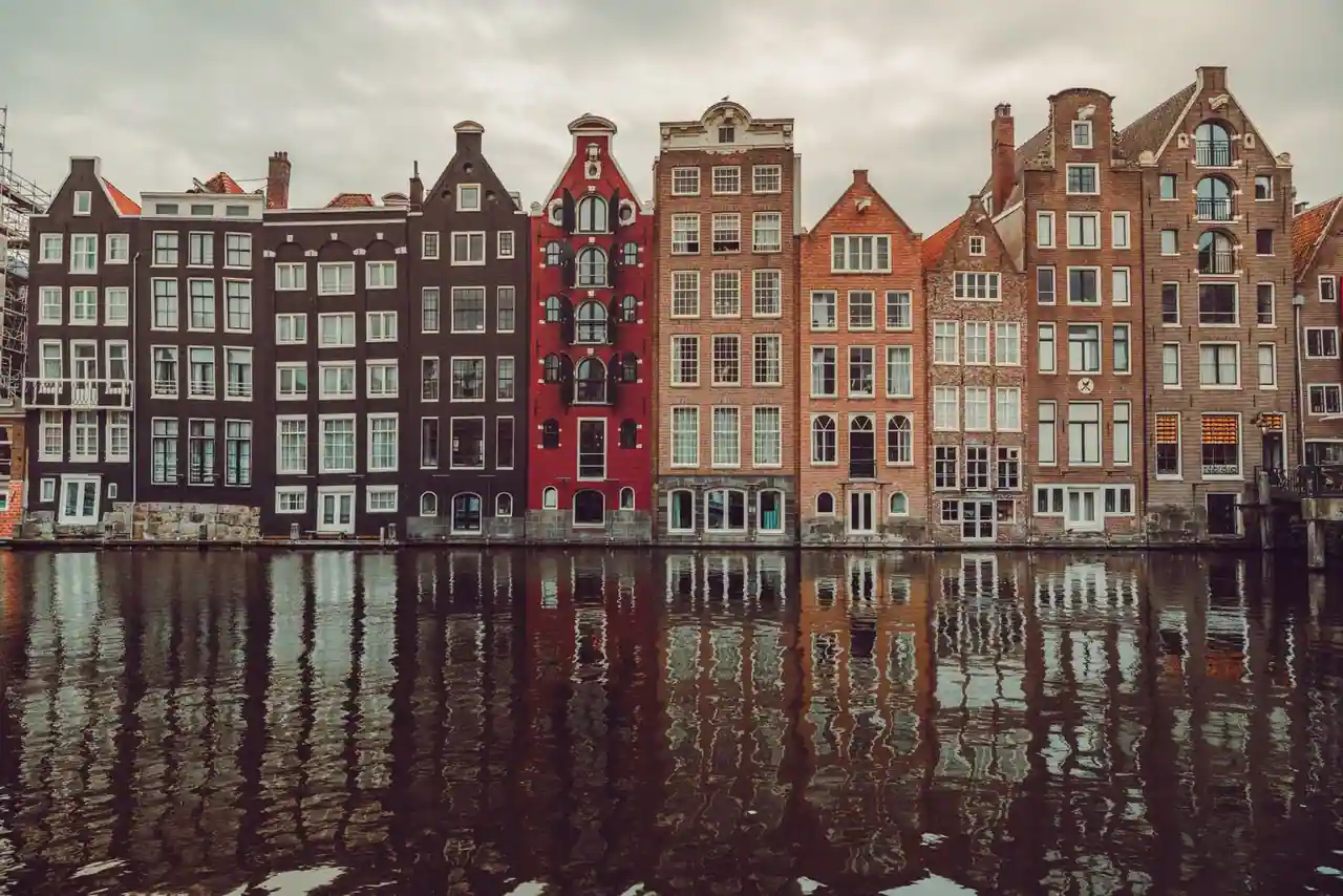 Façades étroites et colorées typiques bordant un canal d'Amsterdam, reflétées dans l'eau.