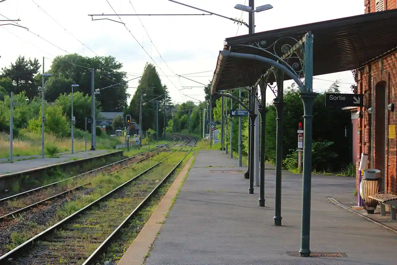 Le quai d'une petite gare régionale française, abrité par une marquise ancienne en fer forgé.