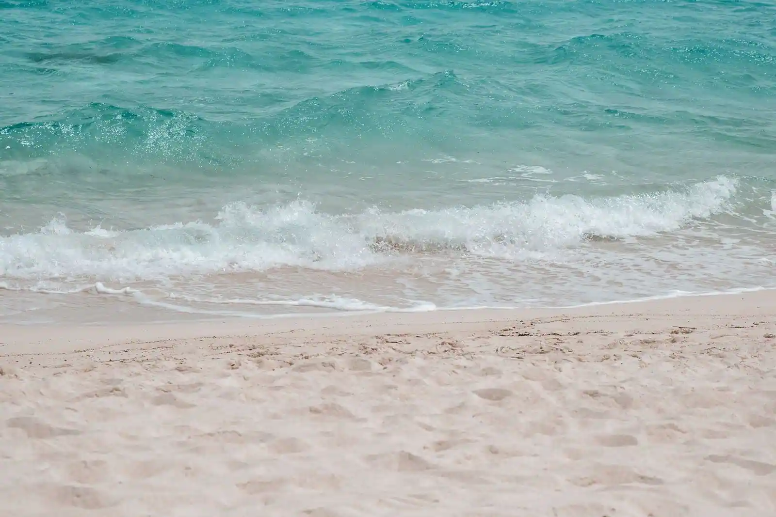Plage de sable clair et vague se brisant sur une mer turquoise