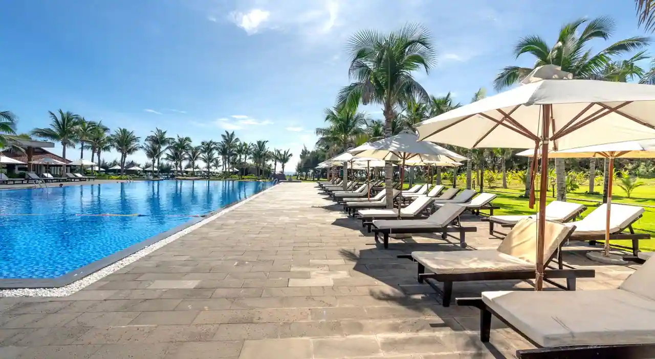 Piscine d'un complexe hôtelier ensoleillé bordée de transats et de palmiers, dans une ambiance de séjour de vacances