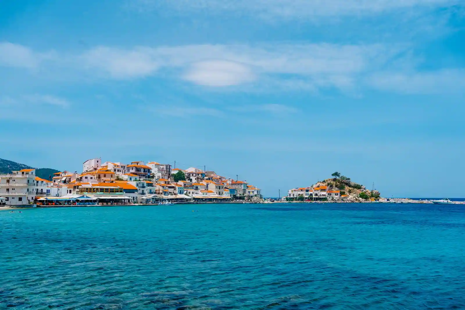 Village grec en bord de mer aux maisons à toits de tuiles orangées, surplombant une eau turquoise