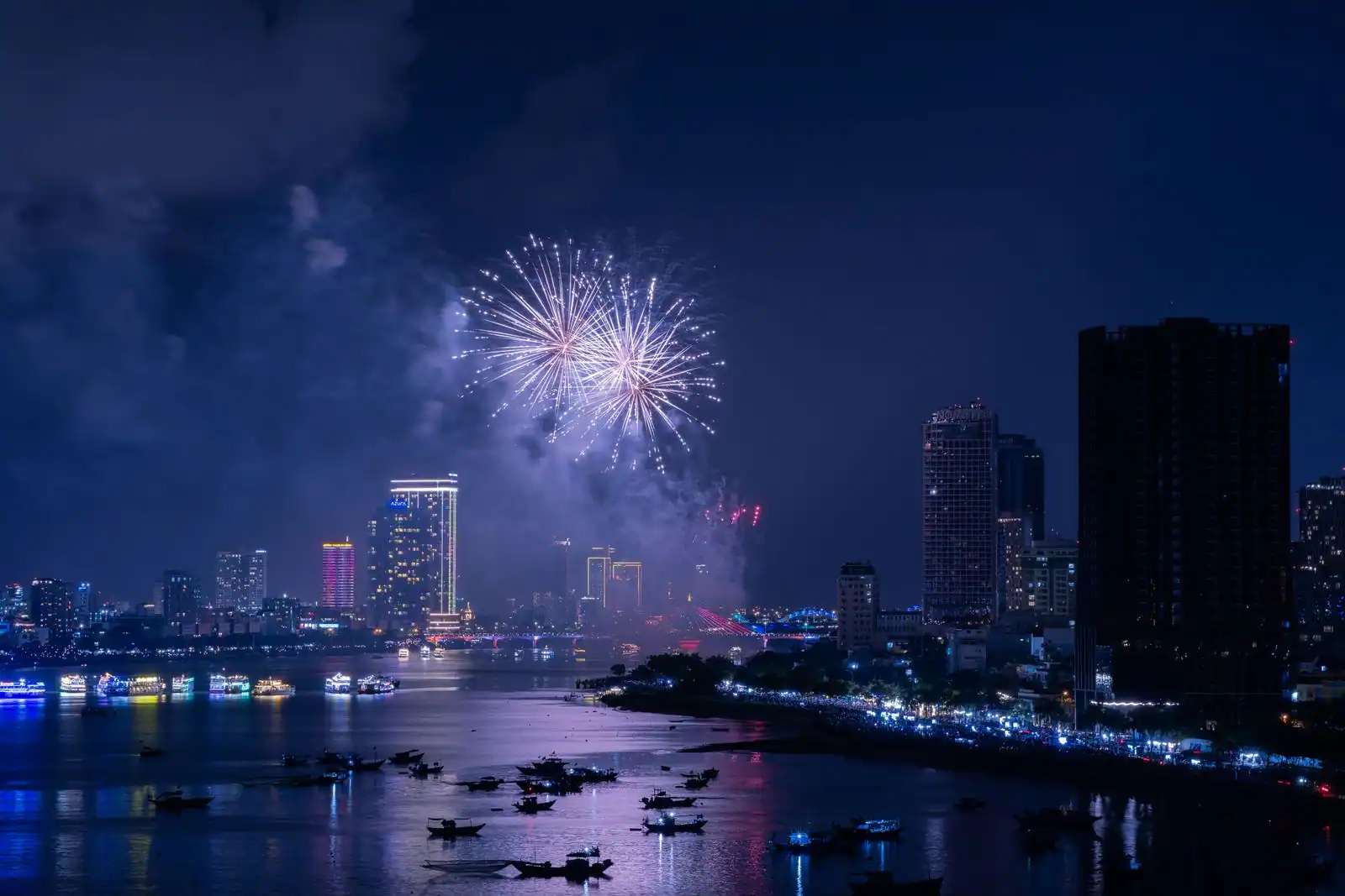 Feu d'artifice illuminant le ciel au-dessus d'une ville et de son front de mer pendant la nuit.