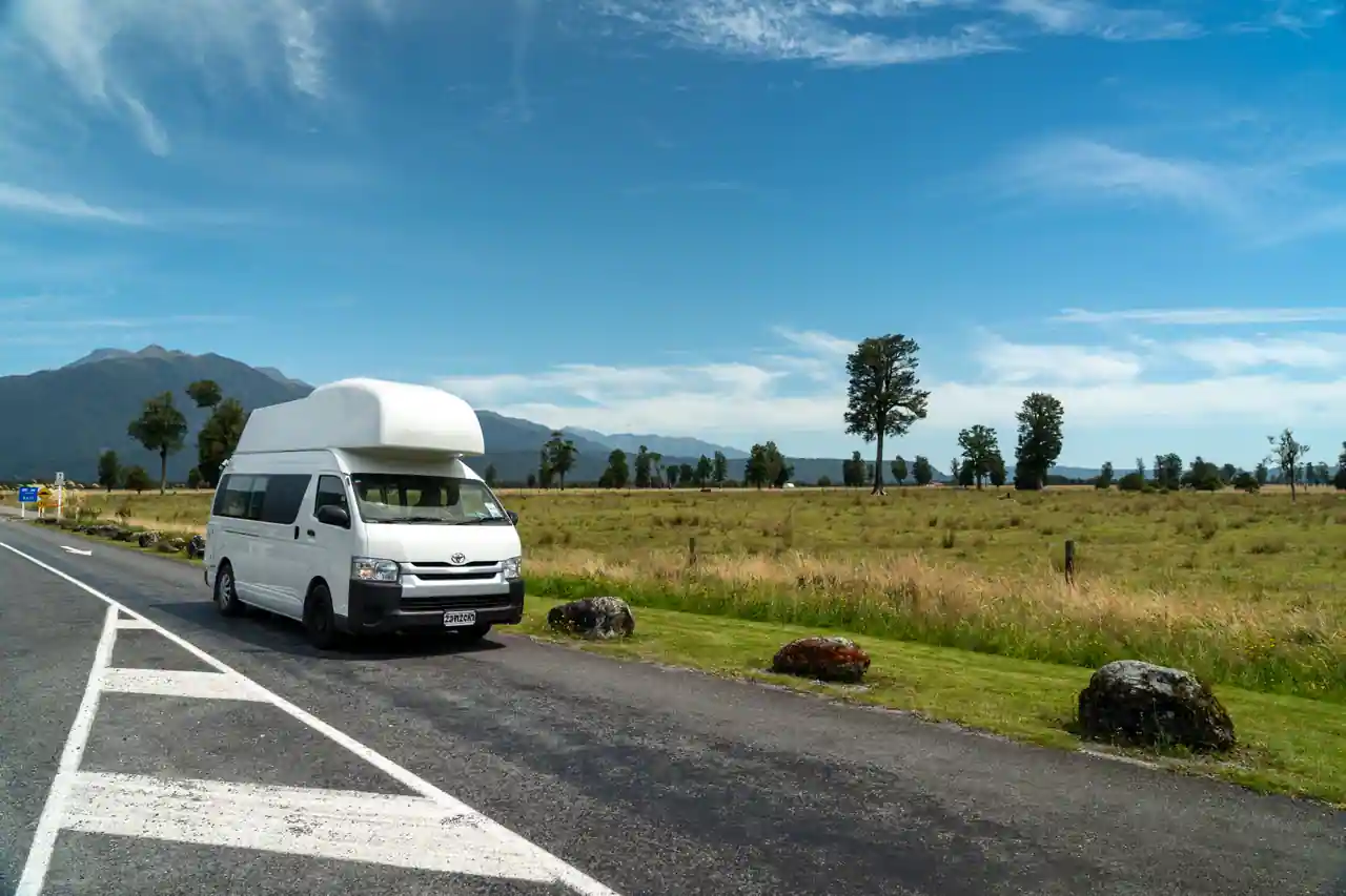 Van aménagé stationné au bord d'une route de campagne, prêt pour un road trip en Europe