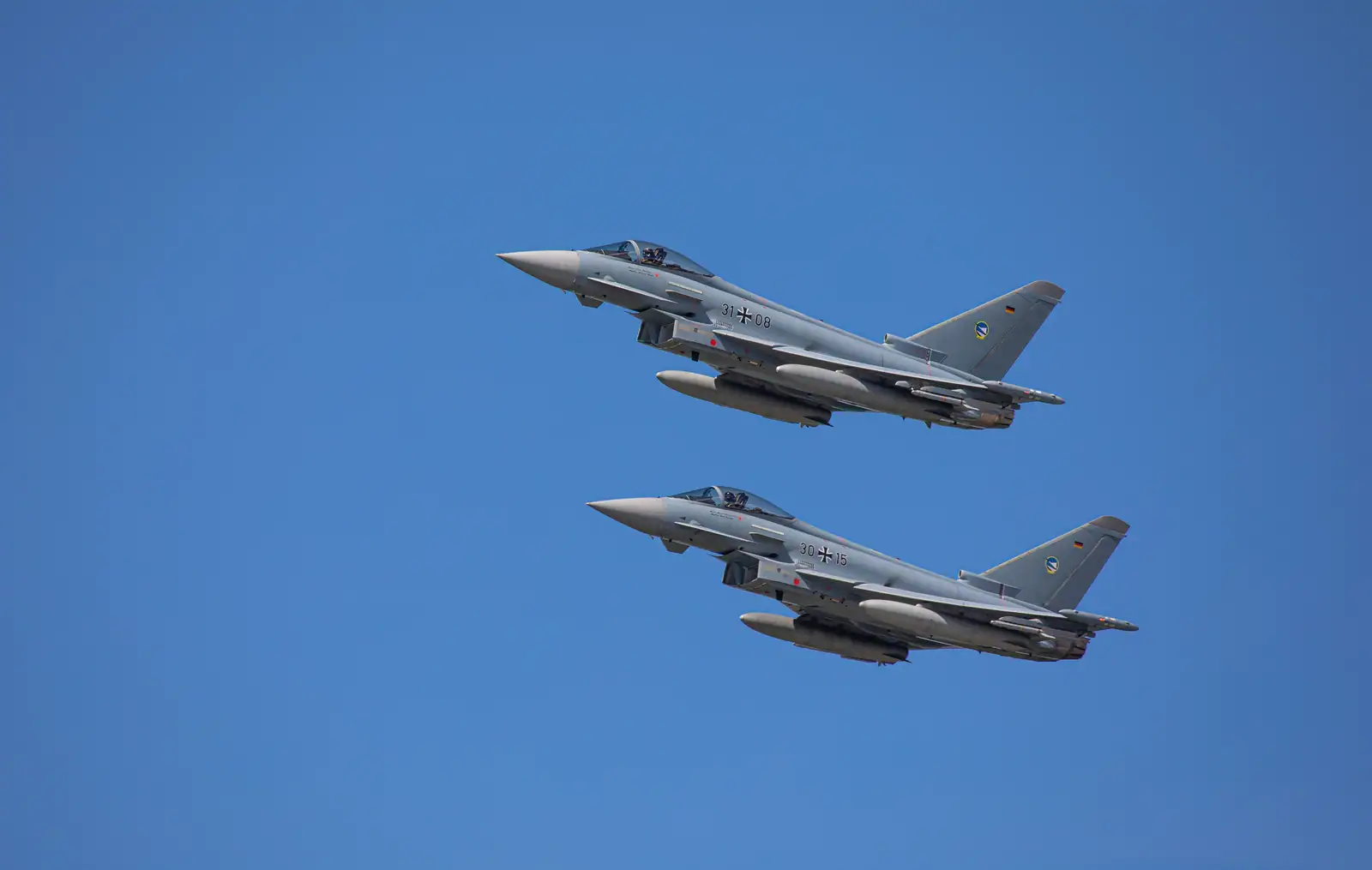Deux avions de chasse en formation dans un ciel dégagé, réservoirs et charges sous la voilure.