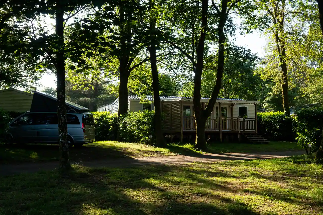 Mobil-home à terrasse en bois sur un emplacement de camping ombragé par de grands arbres