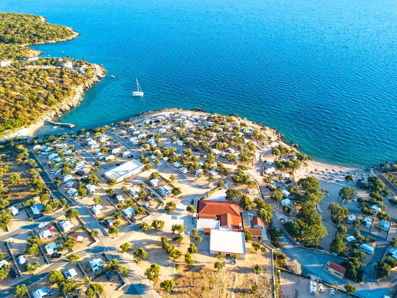 Vue aérienne d'un camping de bord de mer méditerranéen, emplacements et mobil-homes entre pins et plage.