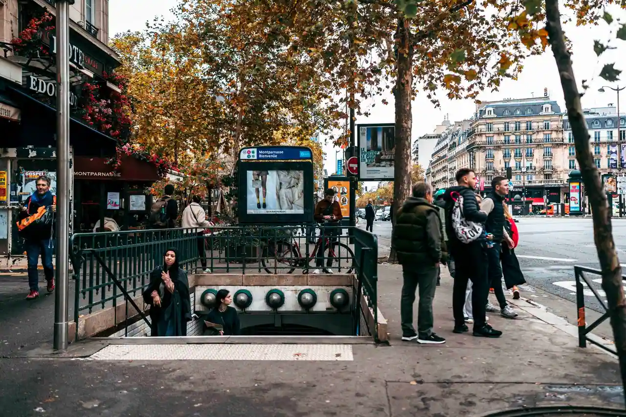 L'entrée d'une station de métro parisienne, son escalier et sa signalétique, avec des passants sur le trottoir.