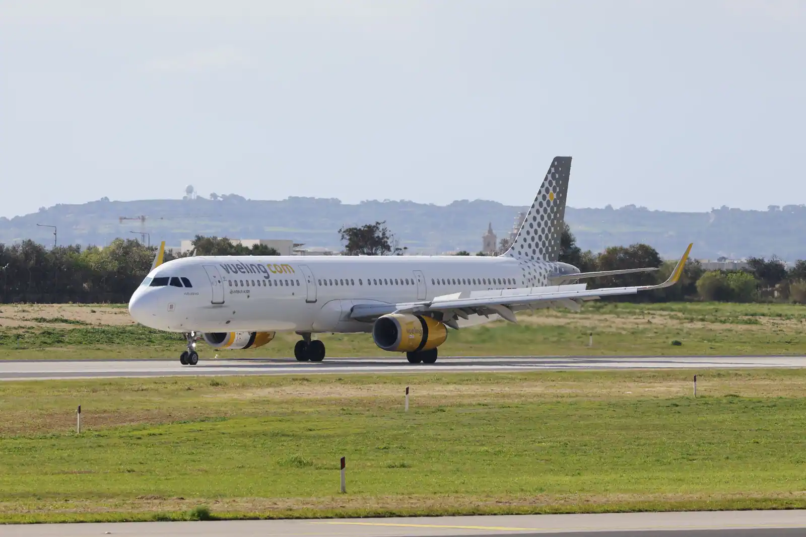 Airbus A321 aux couleurs de Vueling au roulage sur la piste, réacteurs jaunes et dérive à pois.