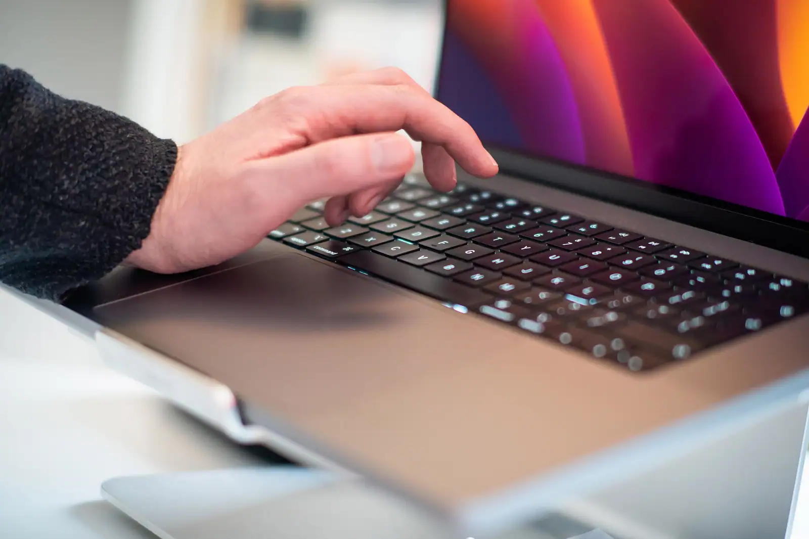 Main posée sur le clavier d'un ordinateur portable ouvert sur un poste de travail clair
