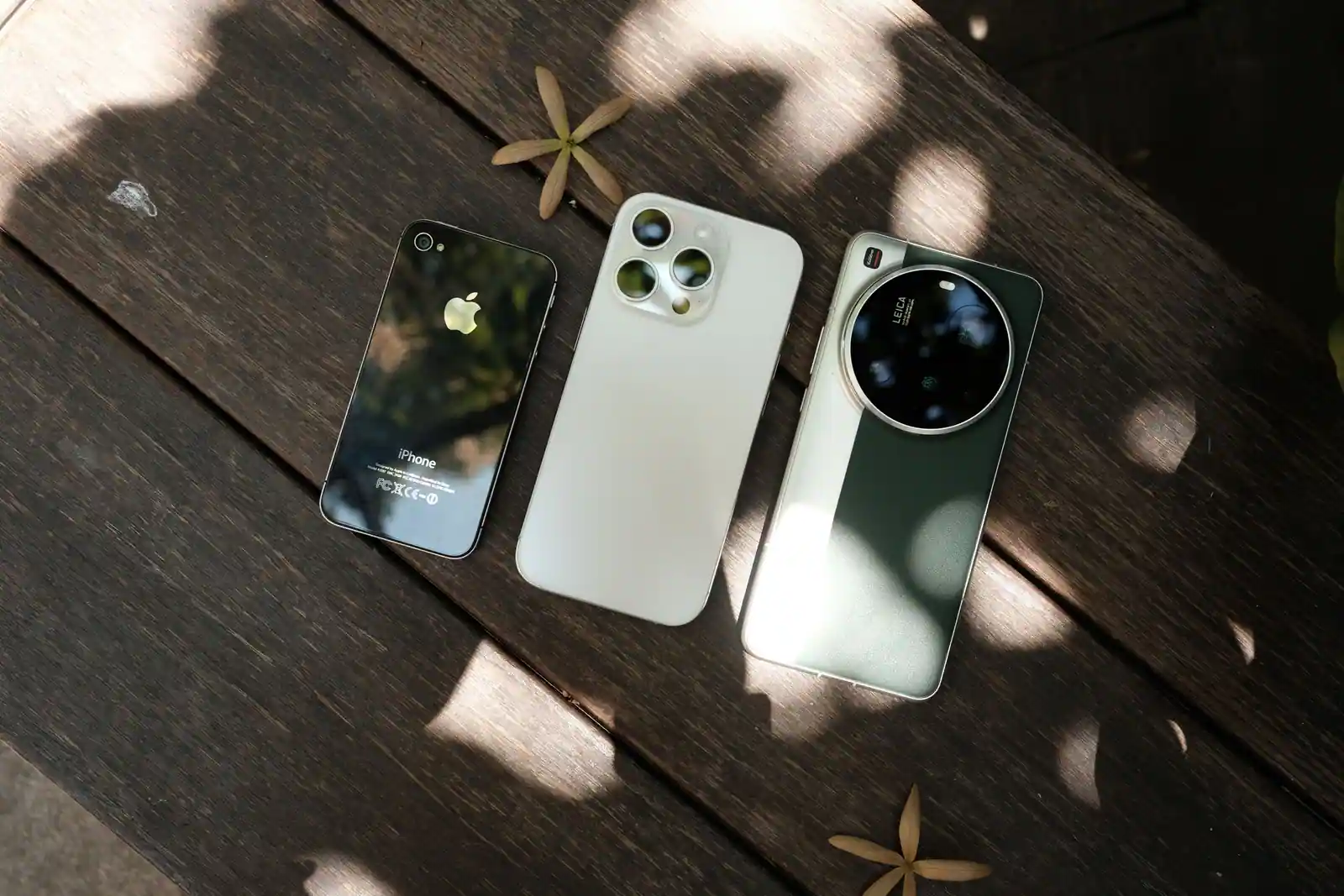 Trois téléphones de marques et de générations différentes, alignés dos visible sur une table en bois.