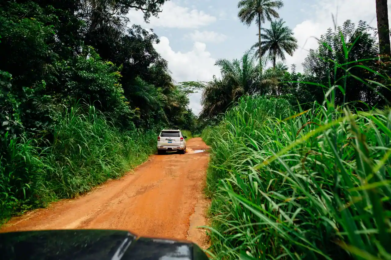 Un véhicule tout-terrain progresse sur une piste de terre ocre bordée d'une végétation tropicale dense.