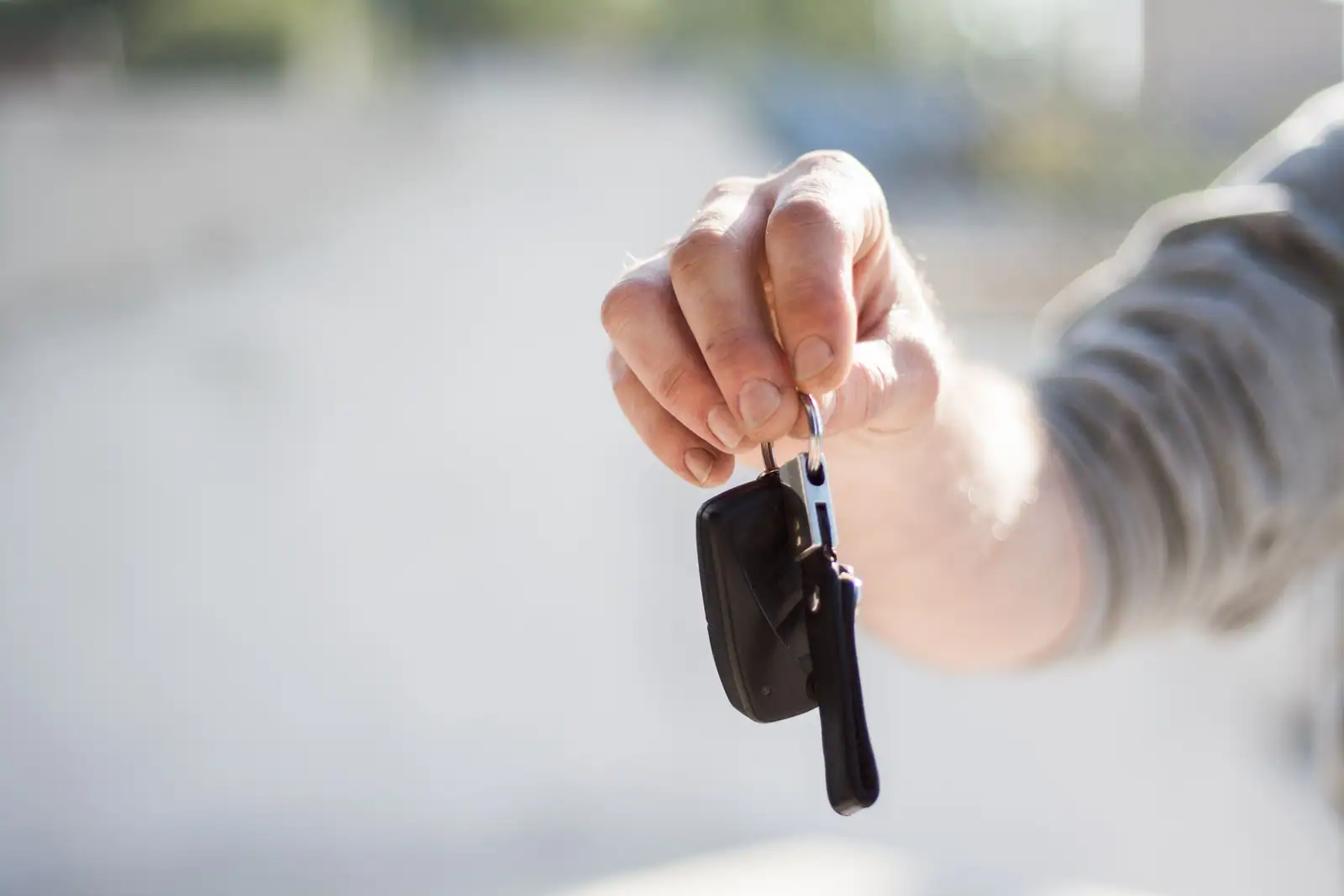 Une main tend une clé de voiture et sa télécommande, au moment de la remise d'un véhicule de location.