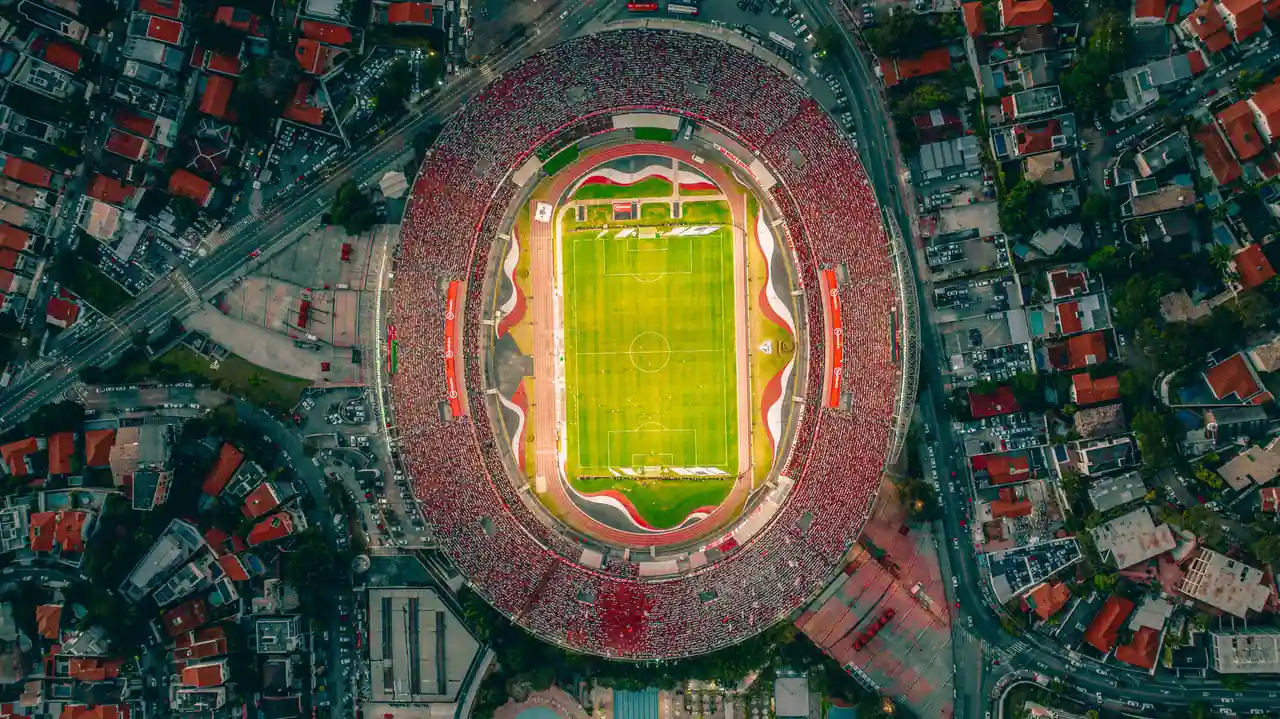 Vue aérienne d'un stade de football comble, cerné par les toits d'un quartier urbain dense.