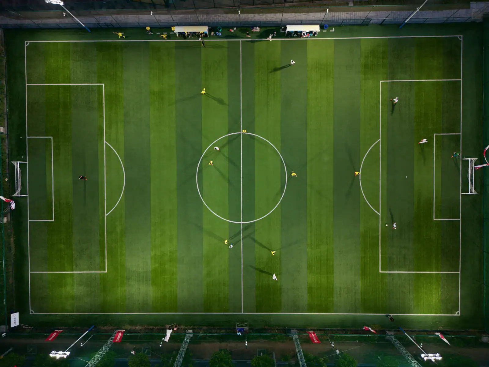 Vue aérienne d'un terrain de football éclairé, avec quelques joueurs dispersés sur la pelouse.