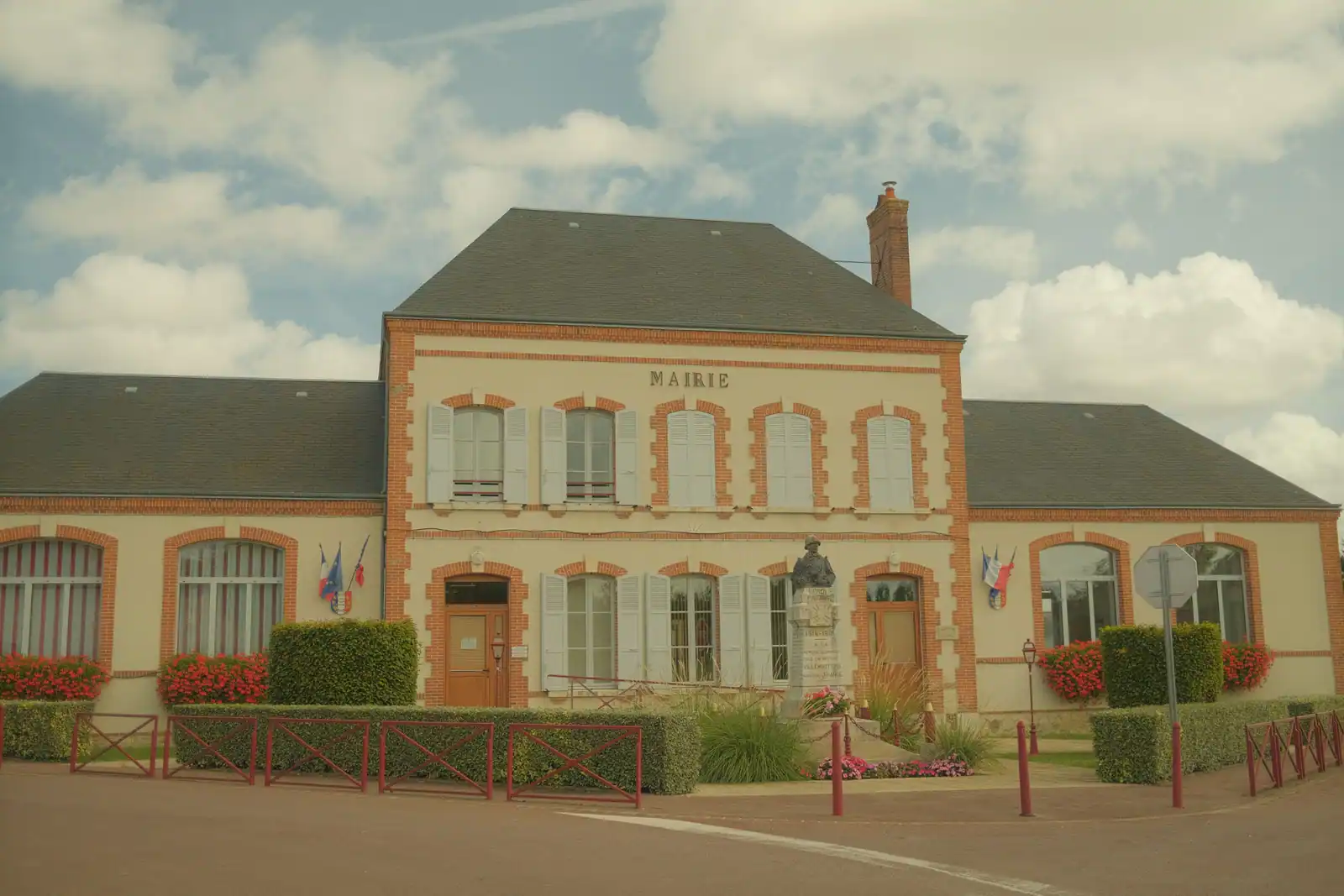Façade d'une mairie de village française, drapeaux tricolores et massifs de fleurs devant l'entrée